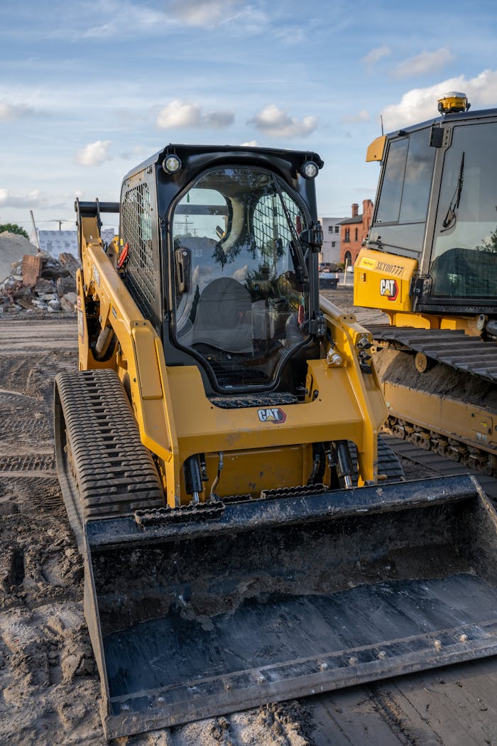 Close-up of a yellow compact track loader on a construction site during daytime.